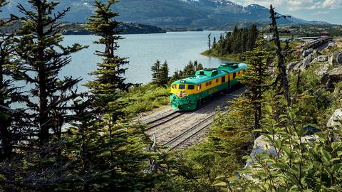 Eine Eisenbahn, die durch Alaska fährt, im Hintergrund Berge.