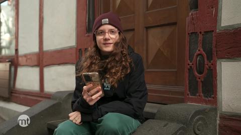 Junge Frau sitzt auf Treppe und hält Handy in der Hand