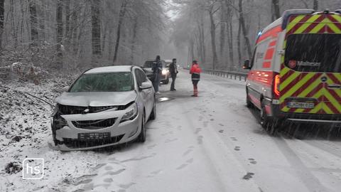 Ein frontal beschädigtes Auto steht am Rand einer verschneiten Straße, daneben ein Rettungswagen.