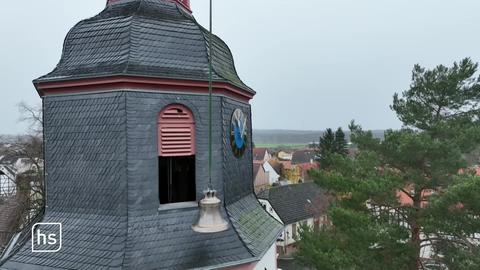 Eine Glocke wird mit einem Kran durch ein schmales Fenster in einem Kirchturm gehoben.