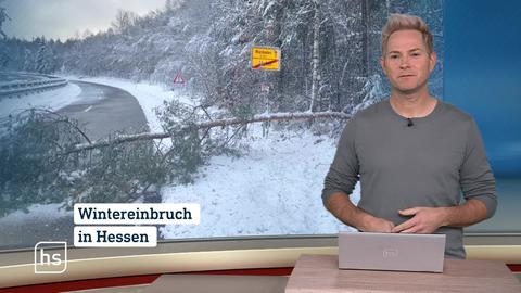 Moderator im Studio vor Bild mit schneebedeckter Straße und umgestürztem Baum.