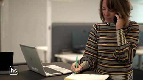 Frau telefoniert während die vor ihrem Laptop steht.