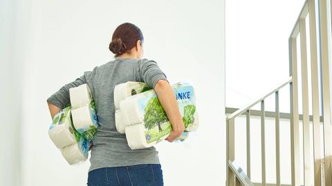 Eine Frau voll bepackt mit Klopapier steigt eine Treppe hoch. 