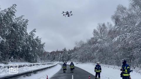 Feuerwehrmänner lassen Drohne über verschneiter Straße und Wald fliegen.