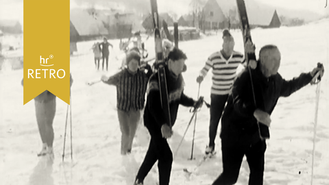 ARD Retro Skikurs Rhön: Die Ski-Schüler*innen mit geschulterten Ski-Brettern auf dem Weg zum Berg.