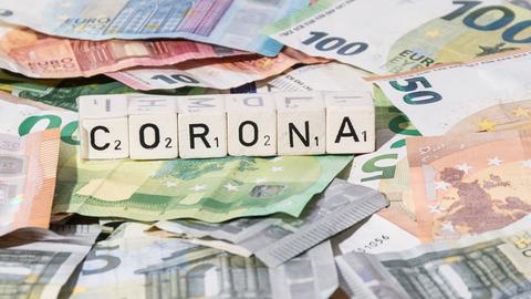 Viele Euroscheine und Scrabbelsteine, die das Wort Corona bilden.