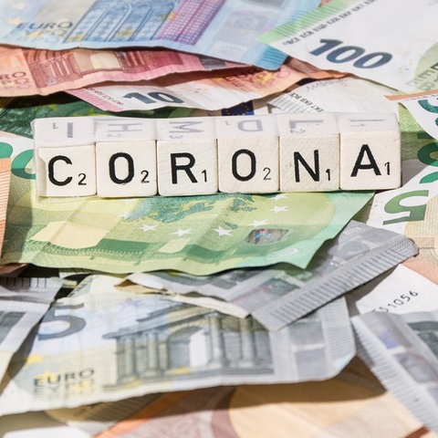 Viele Euroscheine und Scrabbelsteine, die das Wort Corona bilden.