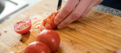 Eine Frau schneidet auf einem Holzbrett Tomaten klein.