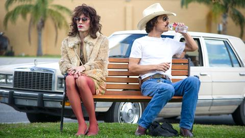 EIne Frau und ein Mann mit Cowboy-Hut sitzen auf eine Bank. Der Mann trinkt aus einer Wasserflasche. Im Hintergrund ein Oldtimer-Auto.