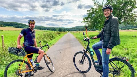 Männer mit Fahrradhelm auf E-Bikes, im Hintergrund ein Radweg.