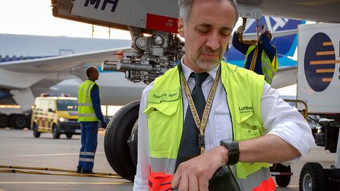 Der Operations Agent guckt auf seine Uhr. Im Hintergrund der A380 der Lufthansa.