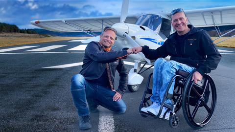 Friso kniet auf dem Boden, neben ihm Christian Thiel im Rollstuhl. Im Hintergrund ein Flugzeug.