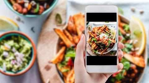 Eine Hand mit Smartphone fotografiert appetitliches Essen.