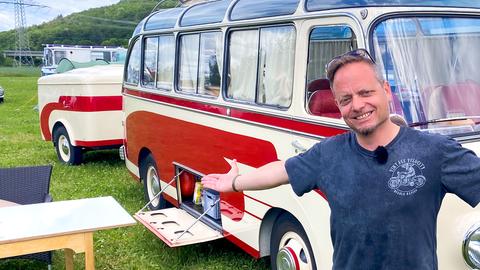 Friso Richter steht strahlend und mit ausgebreiteten Armen vor einem älteren Modell eines Campingvans.