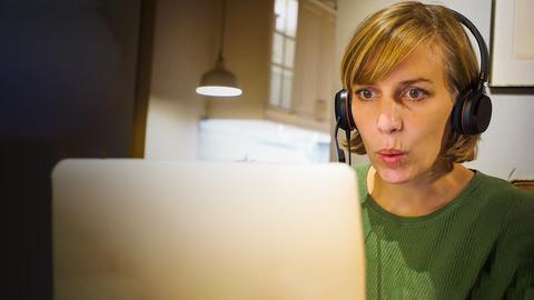 Eine Frau sitzt mit Kopfhörern vor ihrem Laptop und spitzt die Lippen: Sie macht eine virtuelle Übung für Stotterer.