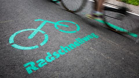 Radfahrer fahren auf einem Radschnellweg an einer Aufschrift auf dem Asphalt vorbei. 