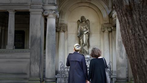 Zwei Frauen vor einer Engelsstatue. 