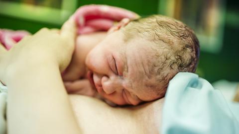 Ein neugeborenes Baby liegt auf dem Bauch der Mutter.
