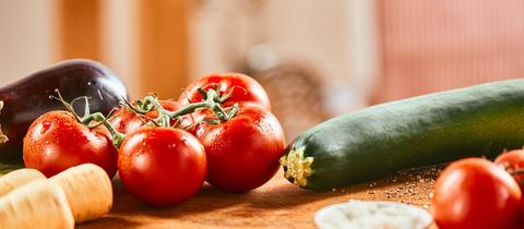 Eine Zucchini und ein Tomatentstrauch liegen auf einer Holzunterlage.