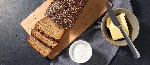 Brot, Butter in Schüssel, Tafelmesser und Salz in Tasse auf Handtuch.