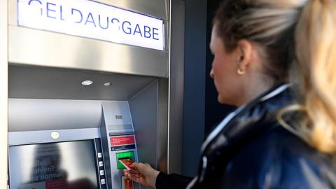 Eine Frau steht vor einem Geldautomat und führt ihre Kreditkarte ein.