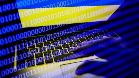 Auf einem Laptop-Bildschirm angezeigte ukrainische Flagge sowie ein Binärcode-Code. 