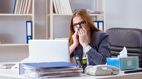 Eine Frau putzt sich die Nase sitzt im Büro