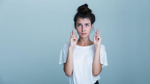 Eine junge Frau guckt nachdenklich und hält die Finger gekreuzt. 