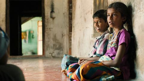 Zwei indische Kinder lehnen sitzend an eine Wand. 