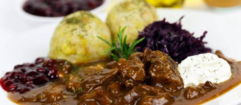 Gulasch, Knödel und Rotkohl auf einem Teller. 