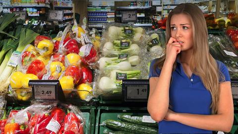 Frau steht vor Gemüseregal im Supermarkt. Das Gemüse ist in Plastik verpackt.