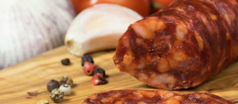 Chorizo auf einem Brett mit Knoblauch und Tomaten im Hintergrund.