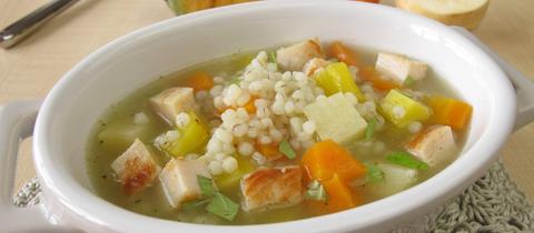 Die Graupensuppe angerichtet in einer Terrine mit den Zuataten Karotte und Pastinake im Hintergrund.