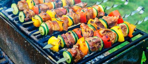 Mehrere Spieße mit Fleisch und Gemüse auf einem Grill.