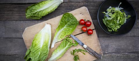 Gehackter und ganzer Römersalat, Taschenmesser und Tomaten auf Holzbrett.