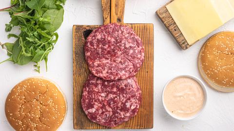 rohes Rinderhackfleisch mit Zutaten und Brötchen, auf weißem Steinhintergrund