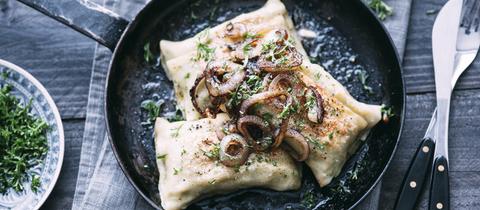 Maultaschen mit Zwiebelschmelze und Petersilie in einer Pfanne.