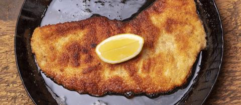 Ein gebackenes Schnitzel mit Zitrone in einer Pfanne. 