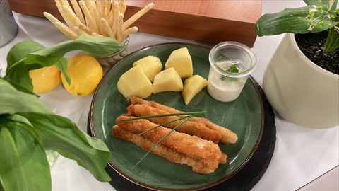 Panierter Spargel und Kartoffeln liegen zusammen mit einem Schälchen Remoulade auf einem grünen Teller.