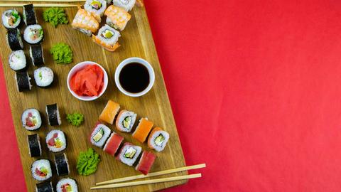 Eine Holzplatte mit einem Set Nigiri-Sushi und Tempura-Rollen sowie Maki- und Uramaki-Rollen auf rotem Hintergrund.