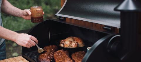 Ein Mann schmiert Rippchen auf dem Grill mit BBQ-Sauce ein