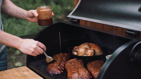 Ein Mann schmiert Rippchen auf dem Grill mit BBQ-Sauce ein