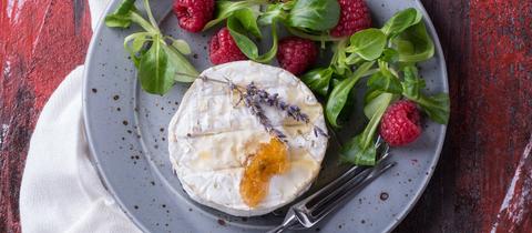 Ein runder Ziegenkäse angerichtet mit Salat, Himbeeren und Brot