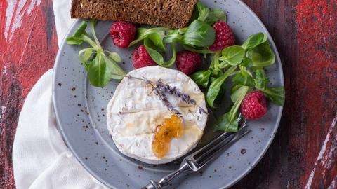Ein runder Ziegenkäse angerichtet mit Salat, Himbeeren und Brot