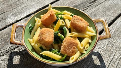 Knoblauchpenne mit Blattspinat und gebackenem Schafskäse auf einem Teller mit Henkeln auf Holzgrund.