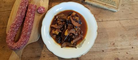 Hutzelsuppe, Ahle Worscht und ein altes Kochbuch stehen auf einem Tisch.