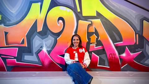 Moderatorin Selma Üsük sitzt vor einer Graffiti-Wand.