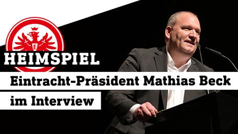 Eintracht-Präsident Mathias Beck an einem Rednerpult, davor links das Eintracht Frankfurt-Logo. Text: Heimspiel - Eintracht-Präsident Mathias Beck im Interview