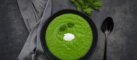 Eine in einem schwarzen Teller angerichtete Erbsen-Minz-Suppe.