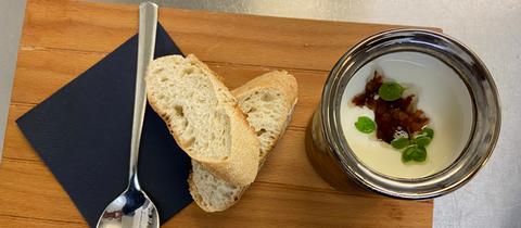 Kohlrabisuppe in Schälchen mit Baguette, Löffel und Serviette auf Holzbrett.